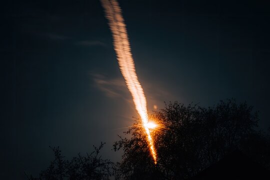 Glowing trail in night sky above trees, light below