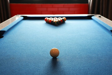 A white ball is placed in the center of the pool table. The balls are arranged in a pyramid for hitting. A blue billiards table has a blur of colorful balls. Billiard balls with numbers on pool table
