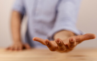 Close-up of a person's hand reaching out, offering assistance or support. Wooden table in the...