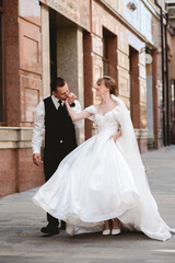 Naklejka premium Happy, sensual newlyweds embrace. A happy bride and stylish groom hold hands and stroll through the city.