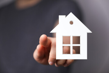 A hand pointing towards a white house model. Illustrating concepts of home ownership, real estate, buying a house, property investment, and drea