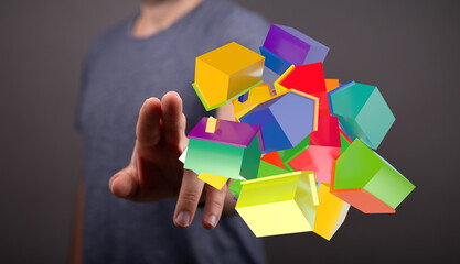 A person's hand is reaching out to touch a collection of colorful, geometric house cubes. The abstract concept of housing, real estate, and prop
