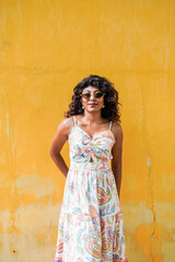 A woman in a white dress stands in front of a yellow wall