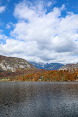 Autumn view of Lake Bohinj in the Julian Alps, Slovenia, featuring vibrant foliage, mirror-like reflections, and tranquil mountain atmosphere.