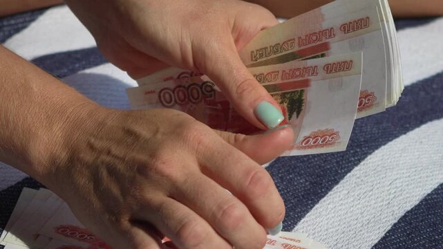 Money, rubles, counting woman's hands meticulously count 5000 ruble banknotes on a striped blanket