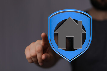 A hand pointing towards a home icon inside a shield, symbolizing security, protection, and real...