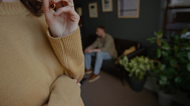 Closeup shot of unrecognizable troubled woman wringing hands and fidgeting with jewelry while standing by window in therapy session, copy space