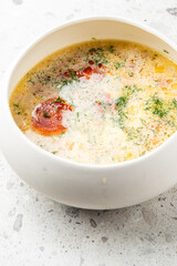 Creamy homemade soup with sausage slices, herbs, and vegetables in a white bowl. Rich yellow broth, rustic presentation, top view on light speckled background.