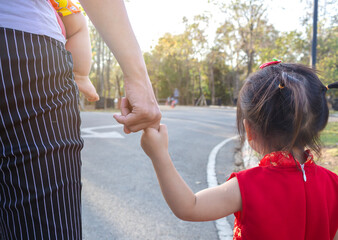 Asian mother and daughter holding hands walking on the road in the park