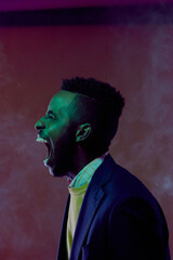 Profile portrait of young stylish Black guy getting rid of negative emotions. Freaked out man expressing his rage by yelling alone in the dark