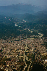 Aerial image of a large city divided by a winding river and surrounded by mountains. Urban areas, bridges, and roads are visible, with distant peaks in the background. Concept of cityscape, geography,