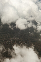 City Landscape Under Thick Clouds from Airplane. Aerial view of a city partially covered by thick white clouds. Urban grid visible through cloud gaps, showing buildings and roads.