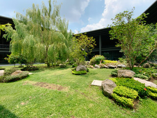 Fototapeta premium Serene modern courtyard garden with lush green grass, weeping willow, and natural rock landscaping offers tranquil business retreat vibes, located in Yogyakarta Indonesia.