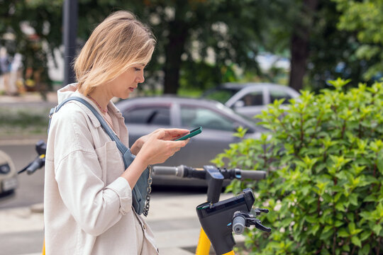 woman using smartphone while standing near electric scooter on city street