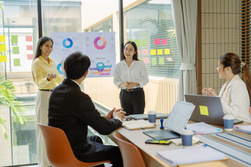 Group of Asian business people presenting data to colleagues in conference room. Business people in suits holding pens pointing at graph documents on table to present company data.