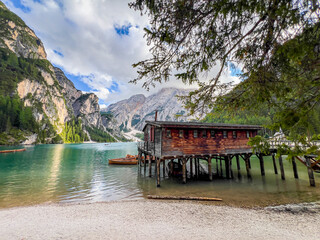 Naklejka premium Lago di Braies or Lake Braies crystal blue lake with wooden rowing boats in Italian Dolomites. Mountain forest lake in Italian alps Dolomites South Tyrol. Woden cabin hut and pontoon above the lake.