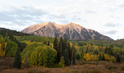 Alpenglow shining on the summit of a peak above Kebler Pass, Colorado, with colorful autumn aspens in the valley below