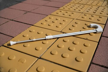 Walking cane resting on tactile paving, offering safety and support for visually impaired individuals navigating urban environments
