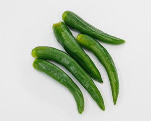 A group of fresh green chili peppers arranged on a clean white surface. Bright, glossy skins suggest crisp, flavorful ingredients ready to spice up sauces, salsas, stews, or healthy dishes