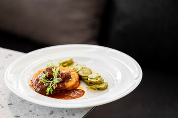 Gourmet vegetable patty with red sauce, grilled zucchini slices, and fresh herbs served on a white plate in a refined dining setting. Top-down view, soft background blur.