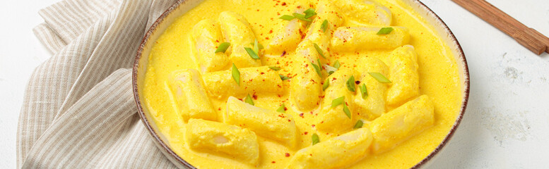 Delicious korean tteokbokki rice cakes served in a creamy cheese sauce, topped with green onion slices, presented in a bowl with chopsticks, authentic food of Korea