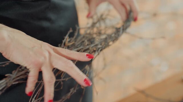 Female florist arranging bundle of thin twigs with hands, creating rustic decoration craft, focusing on natural details, showing handmade artisan floral design process with care in cozy workspace