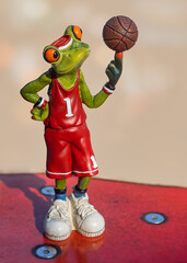 Frog wearing a red basket ball dress and balancing a ball on his finger