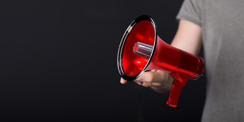 A person holding a red megaphone against a dark background, representing announcement,...
