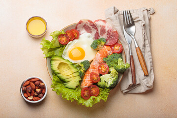 Healthy ketogenic diet concept showing a balanced meal on plate with salmon, avocado, fried egg, bacon, broccoli, tomato, and fresh salad, promoting low carb and high fat eating