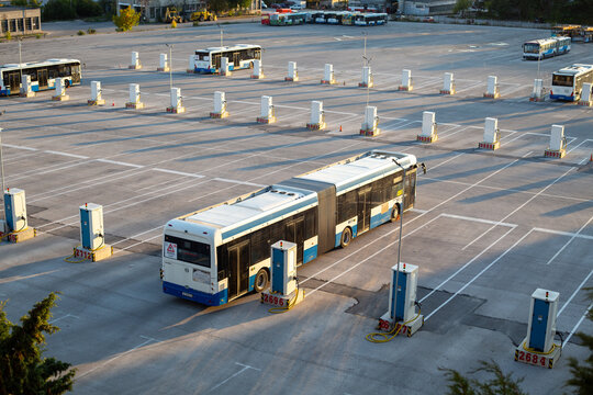 Aerial view of a large depot or parking lot for electric city buses, showing an articulated bus at a charging station with multiple charging points in the background. Varna.  Bulgaria.  20.10.2025
