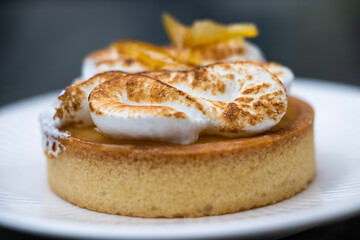 A lemon meringue tart with golden crust and toasted swirls sits elegantly on a white plate