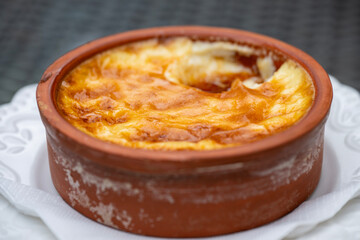 A rustic baked creme brulee with a golden crust rests in a brown ceramic bowl atop a white plate and napkin.