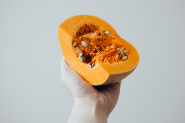 Female hand holding a cut pumpkin on a white, ingredient for a autumn fall dish.