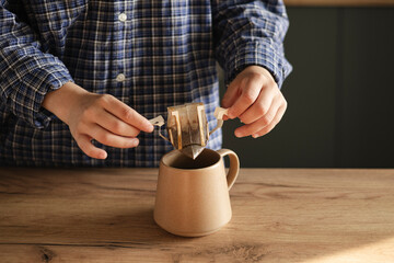 Woman hand holding cup with black coffee and drip filter on kitchen table.