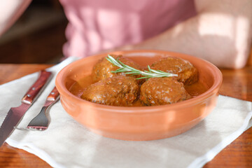 A person eating tuna rolls in tomato sauce served on a clay plate with rosemary on a linen tablecloth. Rustic Mediterranean home-cooked food.