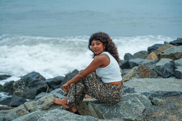 A woman is sitting on a rock by the ocean