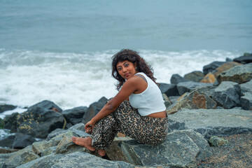 A woman is sitting on a rock by the ocean
