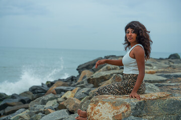 A woman sits on a rock by the ocean, looking out at the water
