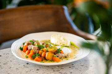 A gourmet dish of tender meat, potatoes, and carrots in a creamy sauce, garnished with fresh herbs, served on a white plate in a restaurant setting.