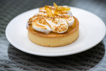 A lemon meringue tart with golden crust and toasted swirls sits elegantly on a white plate