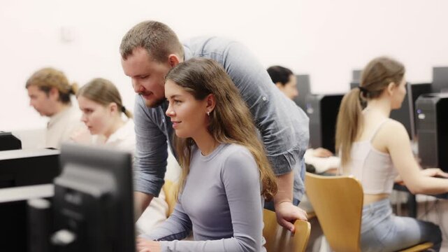 Young male teacher helping young female trainee work at computer in office