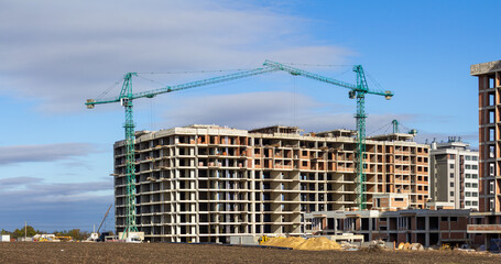 A wide shot of a multi-story residential building under construction, featuring two prominent tower cranes against a bright blue sky, symbolizing urban development, real estate growth, and modern civi