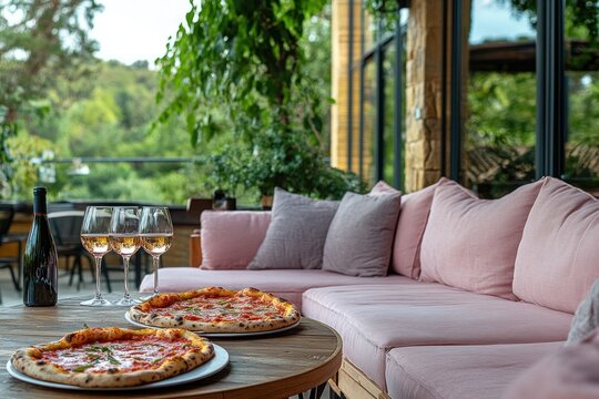 Pizza and white wine on the terrace. Pink sofa with pillows on balcony.