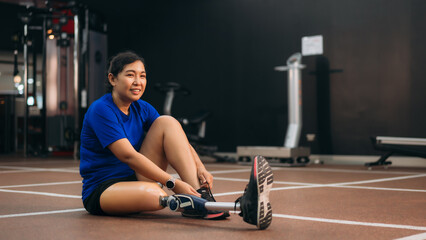Smiling woman with a prosthetic leg stretching on the gym floor, representing fitness, rehabilitation, motivation, and the strength to stay active with a positive and determined mindset.