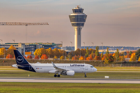 Ein Airbus A320 der Lufthansa rollt &uuml;ber das Rollfeld des Flughafens M&uuml;nchen. Im Hintergrund befinden sich der markante Kontrollturm sowie herbstlich gef&auml;rbte B&auml;ume