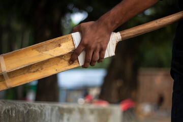 Closeup of a person holding a wooden cricket bat with white tape on the handle