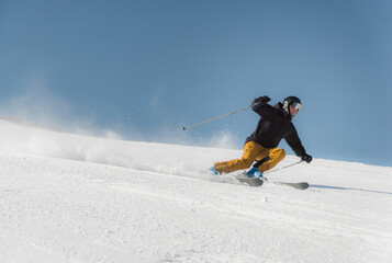 Skier wearing yellow pants gliding fast on fresh snow under clear blue sky, winter sports background ideal for travel and adventure concepts.