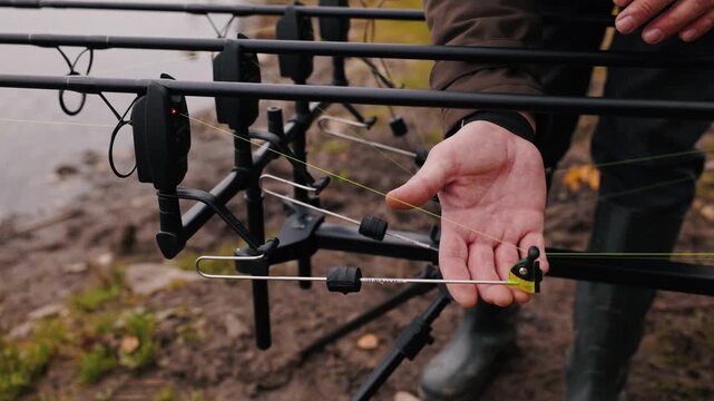 Close-up of fisherman hand installing fishing line on bite alarm and checking setup accuracy, detailed preparation process on autumn lake, professional carp fishing equipment and outdoor recreation