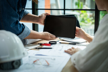 Two people are holding a tablet and a laptop, and they are working on a project. Scene is focused and productive