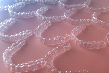 Transparent orthodontic aligners arranged in perspective on pastel blue and pink gradient...